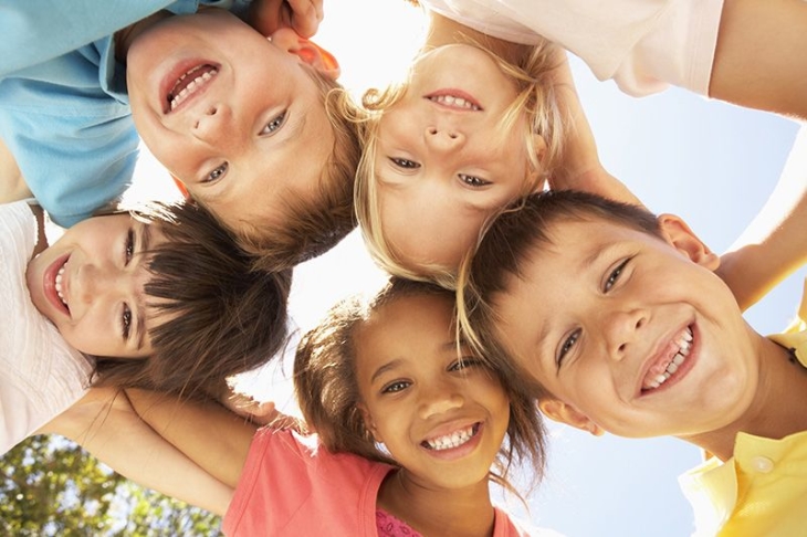 cinq enfants se tiennent par les épaules et regadent en souriant l'appareil photo qui les prend en vue de dessous.